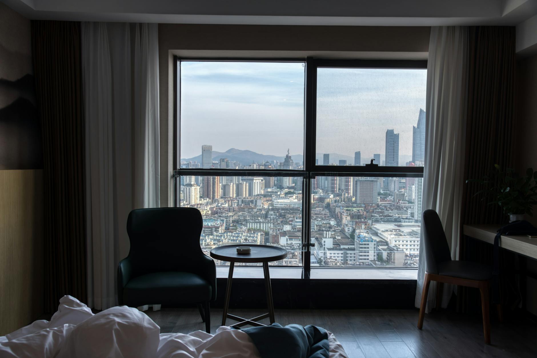 Stylish modern hotel room with floor-to-ceiling windows overlooking a city skyline