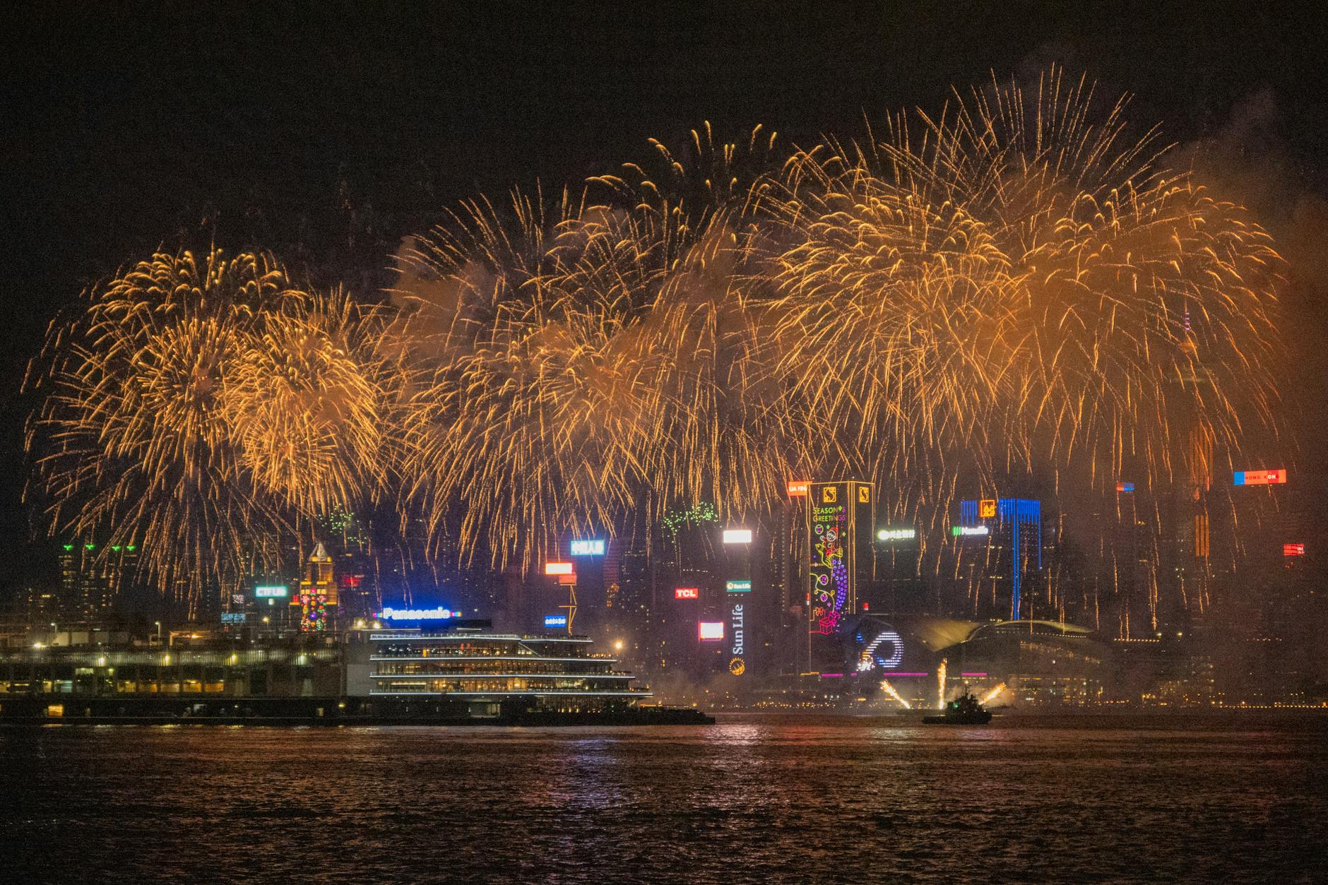 Fireworks exploding over a harbour with city lights reflected in the water