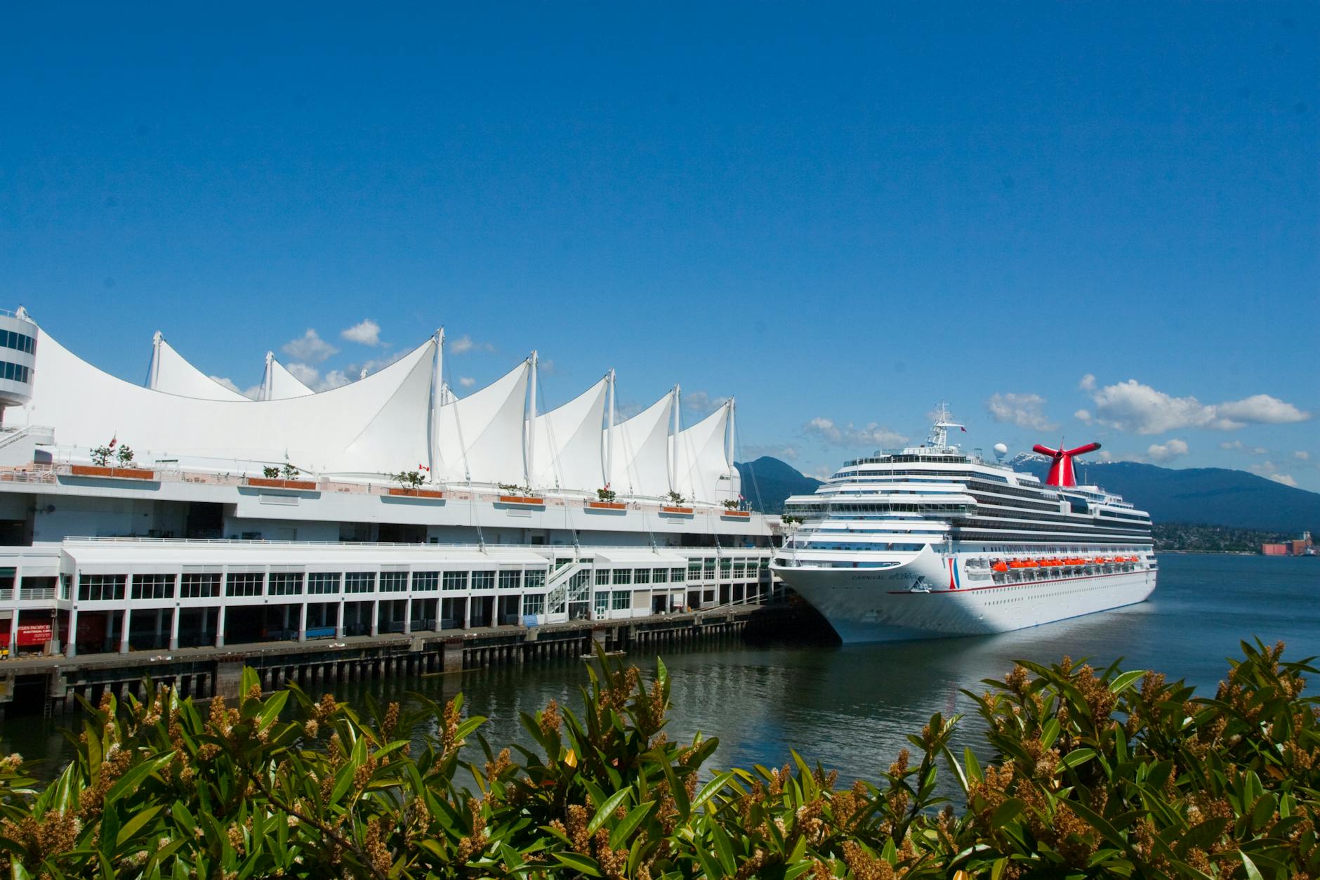 A cruise ship is docked at Canada Place in Vancouver on a sunny day, showcasing the iconic sails.