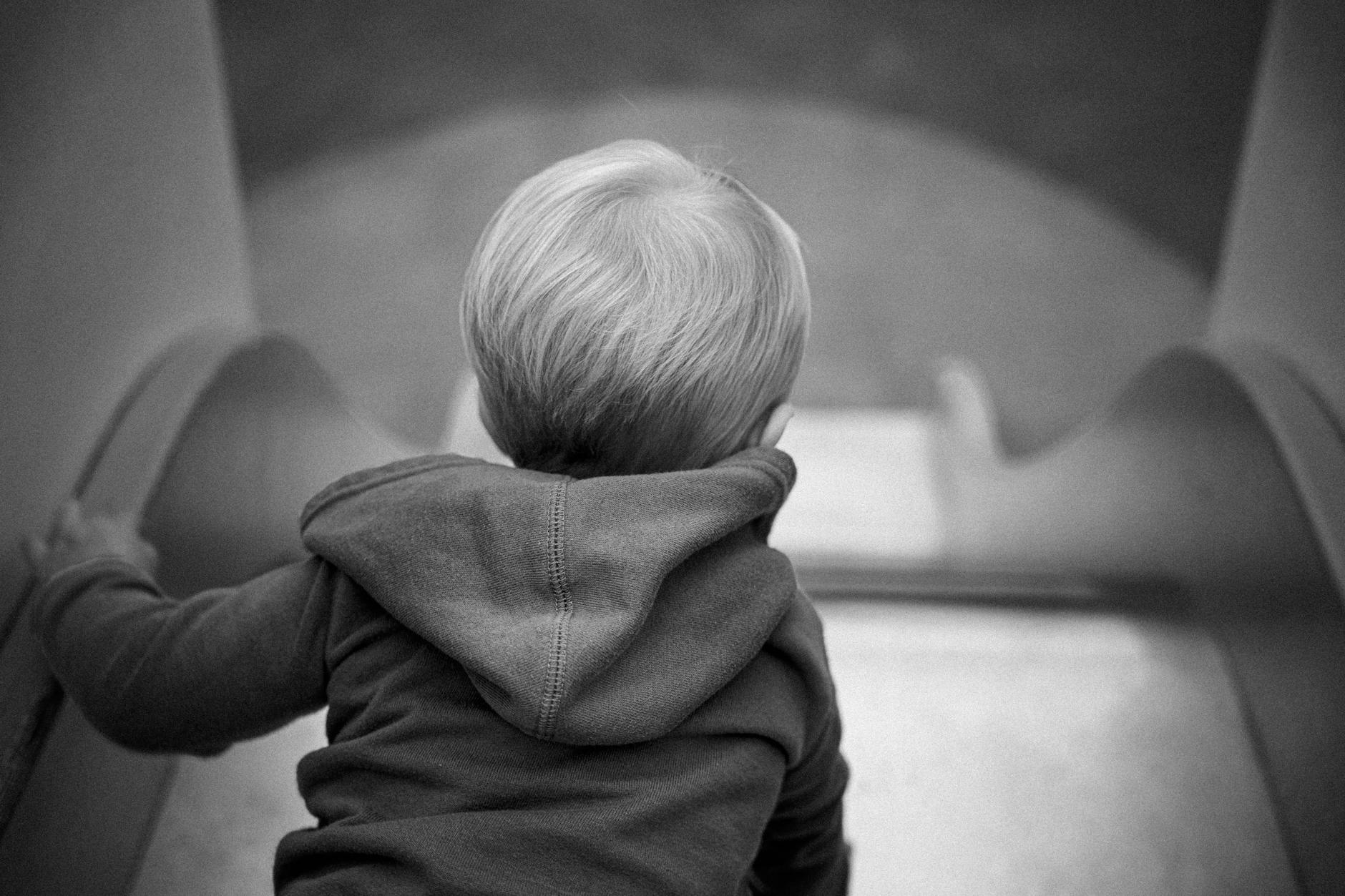Black and white photo of a child crawling up a slide in an outdoor play area.