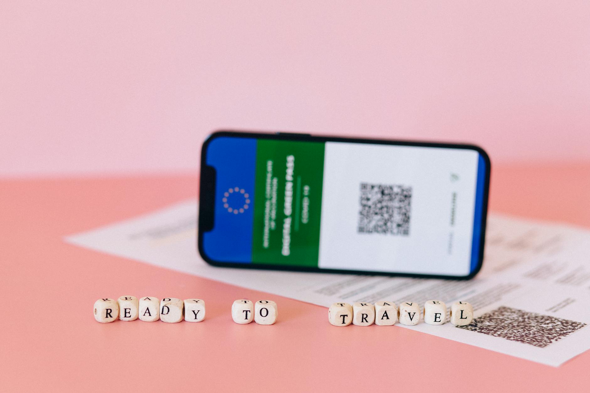 Smartphone displaying digital green pass on a pink surface with travel beads.