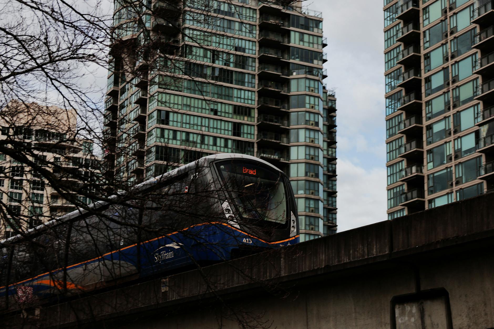 SkyTrain passing modern high-rise buildings in Vancouver, emphasizing urban transit and architecture.
