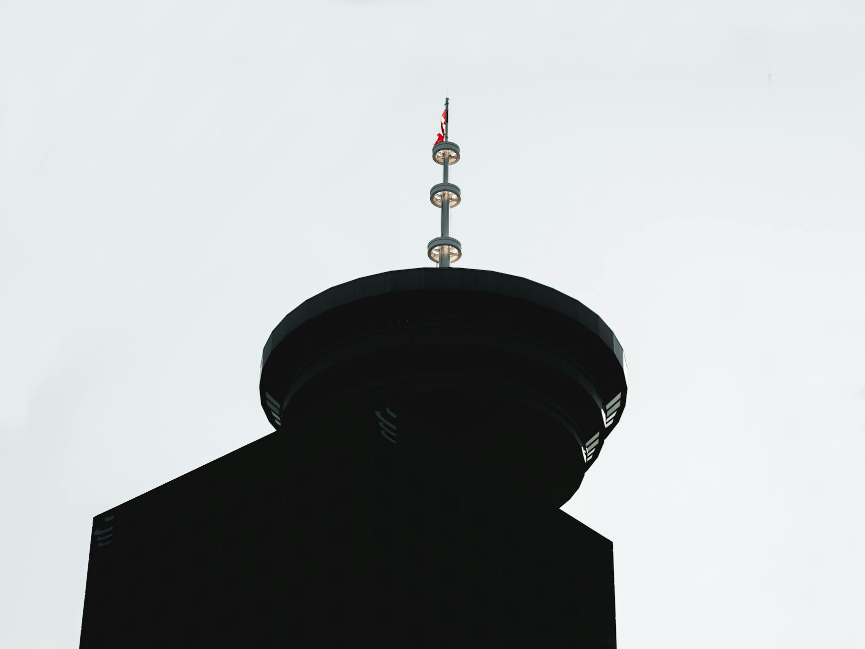 A low-angle silhouette view of Vancouver's iconic Lookout Tower with a flag on top.