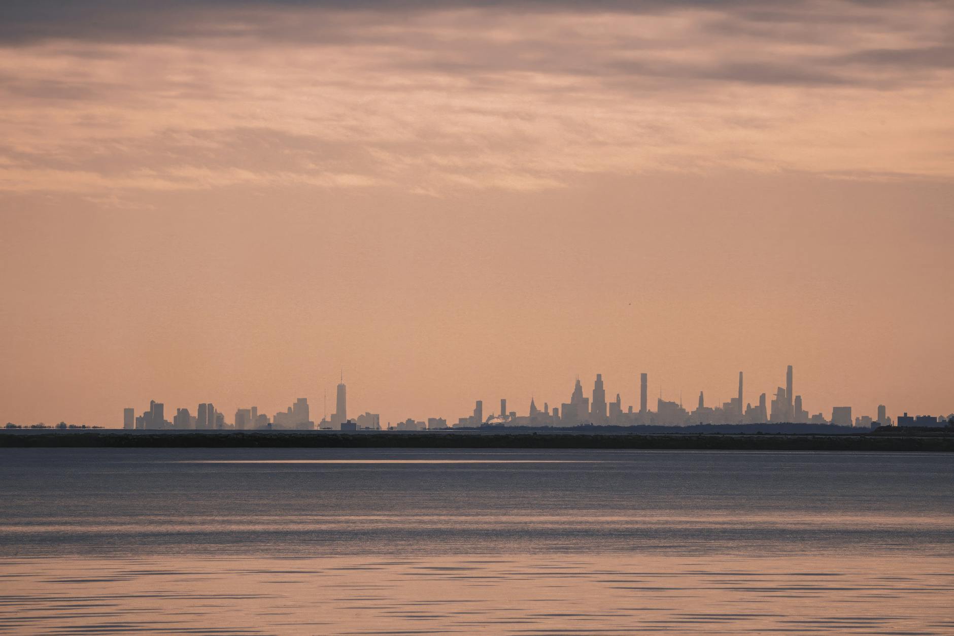 Silhouette of a city skyline against a serene pink sunset over calm waters.
