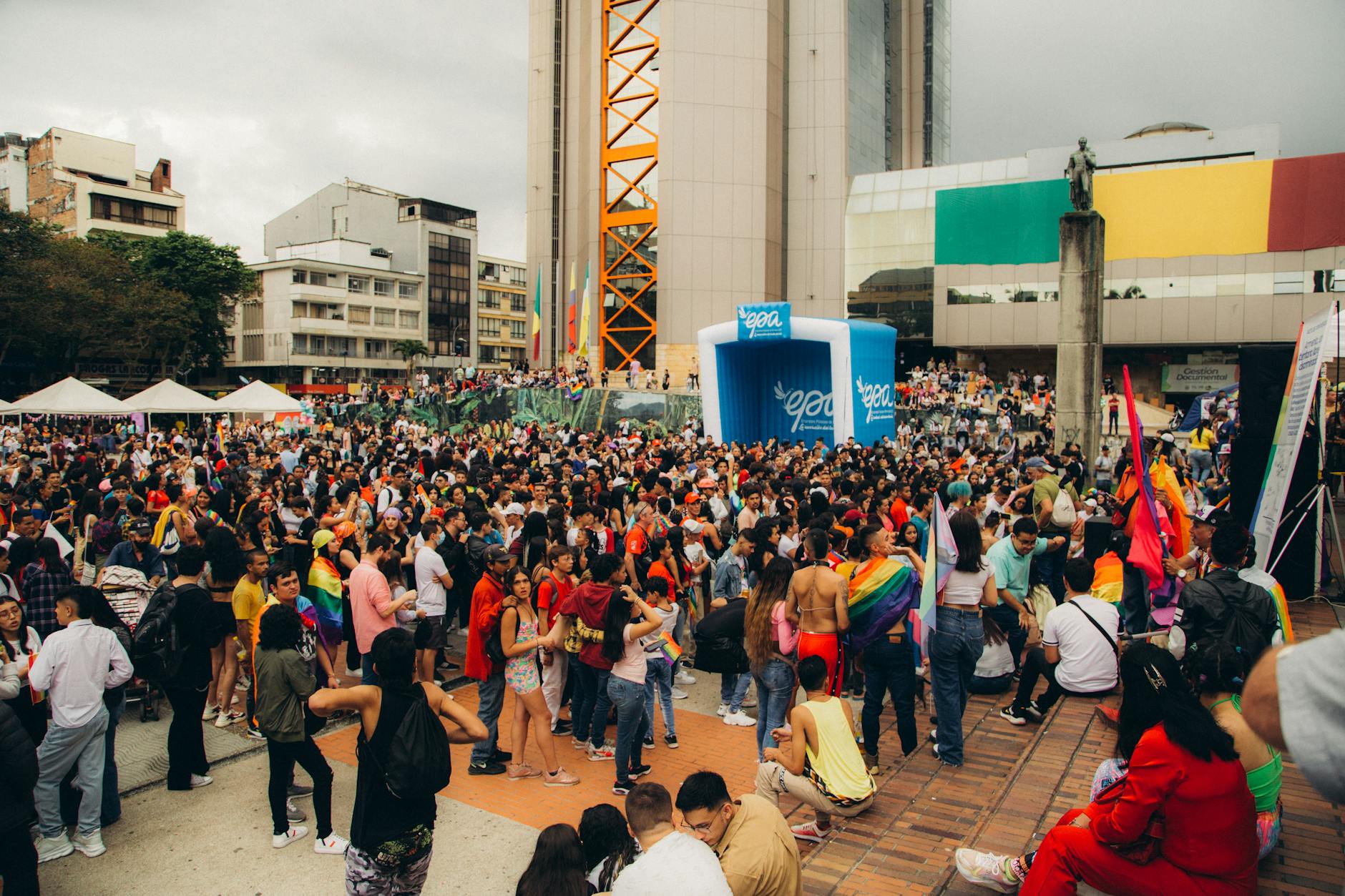 A lively urban gathering with a diverse crowd celebrating with flags in a city plaza.