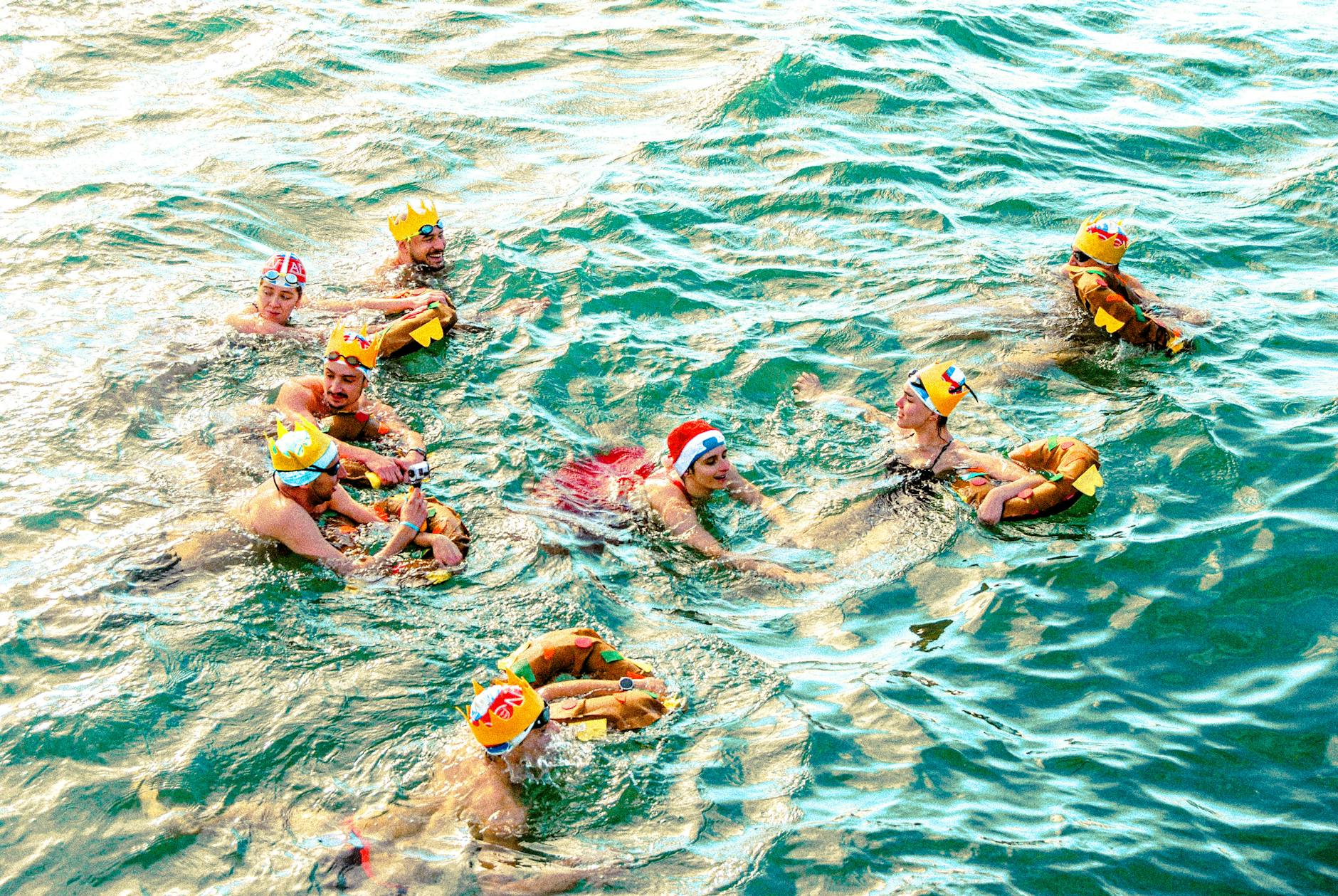 Group of adults swimming in festive hats during a holiday event outdoors.