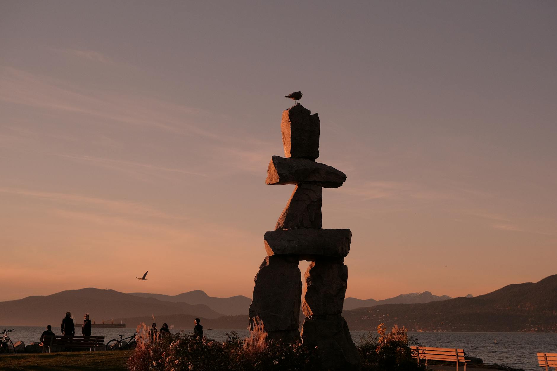 Inukshuk silhouette against a pink sunset sky over a coastal landscape.