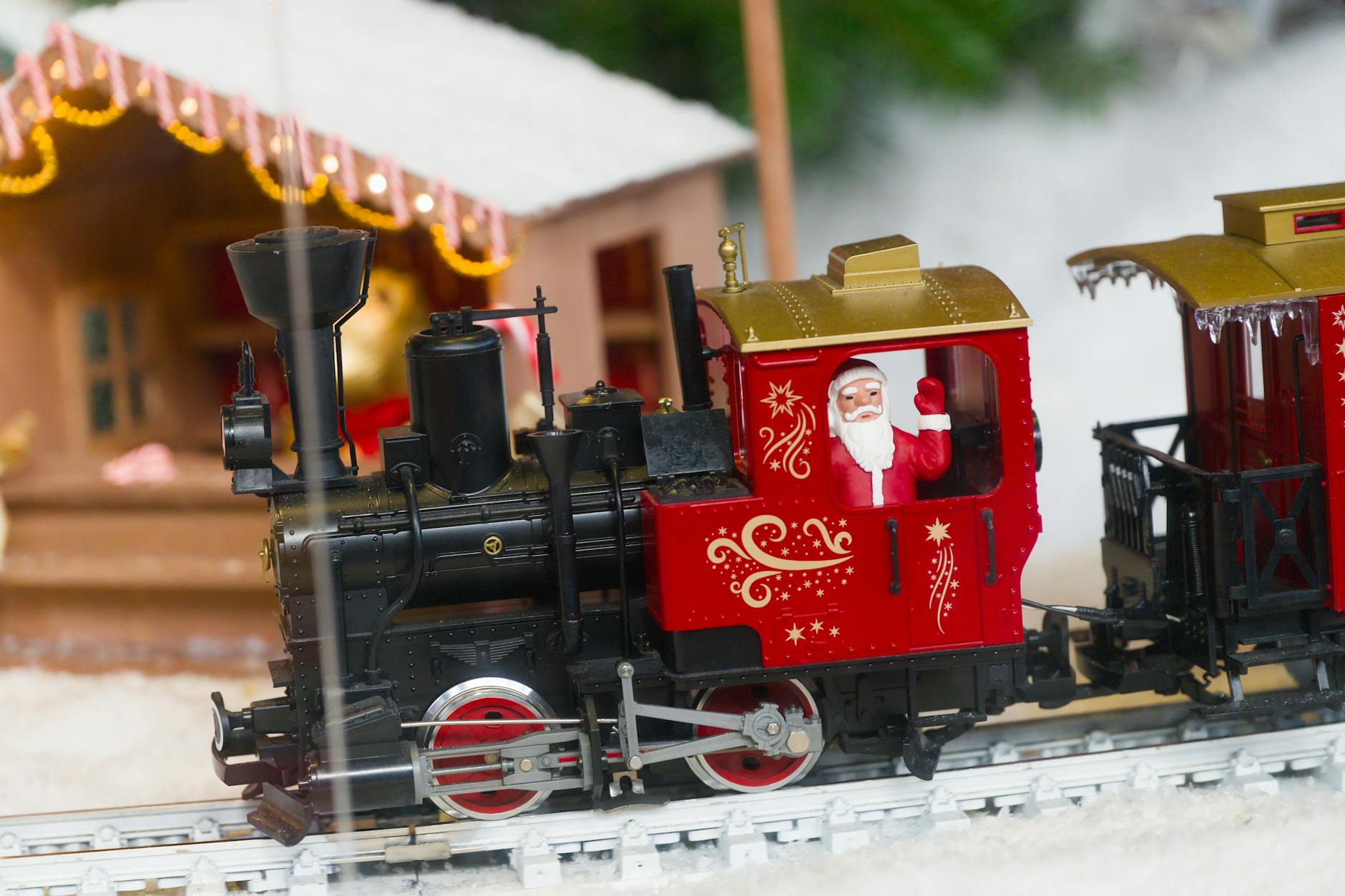 A model train engine with a waving Santa figurine, set on a snowy scene, creating a festive holiday atmosphere.