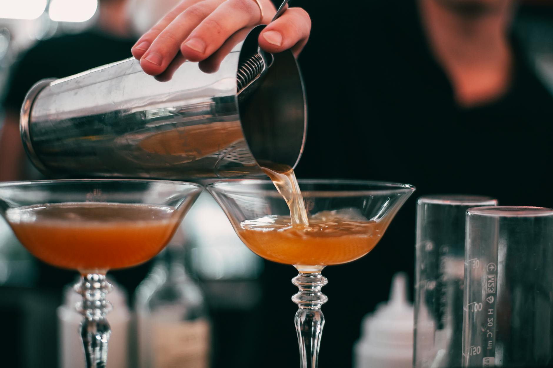 A bartender skillfully pouring cocktails into glasses with a cocktail shaker in a bar setting.