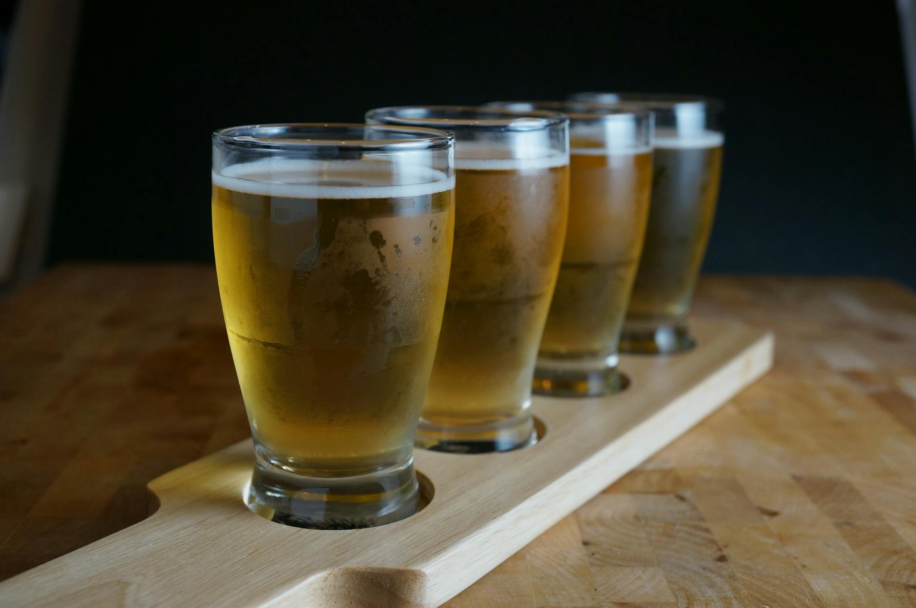 A flight of craft beers served in small glasses on a wooden paddle, perfect for tasting sessions.