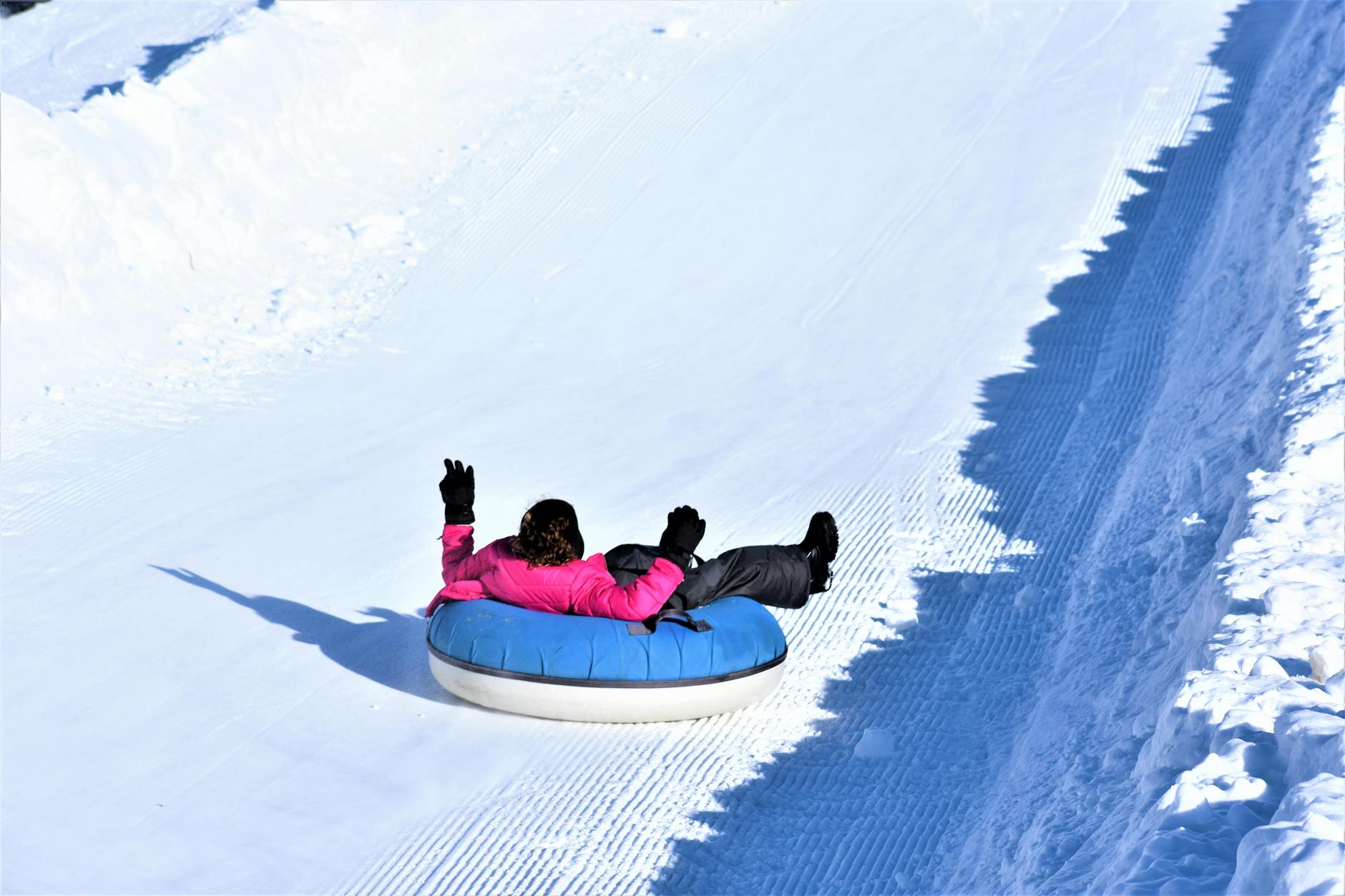 Children sliding down a snowy toboggan run on inner tubes.