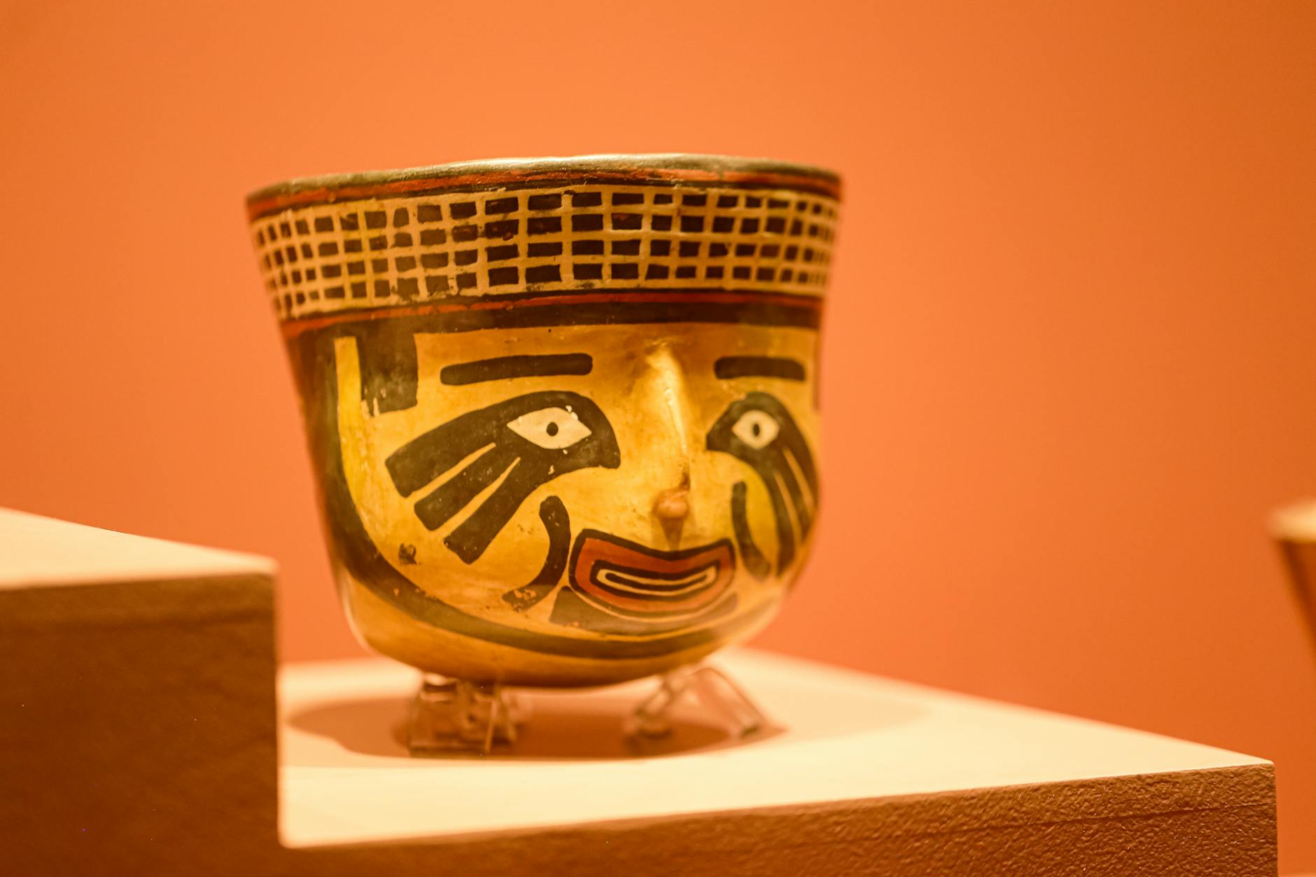 Detailed view of an ancient ceramic vase with a vibrant face design displayed in a museum setting.