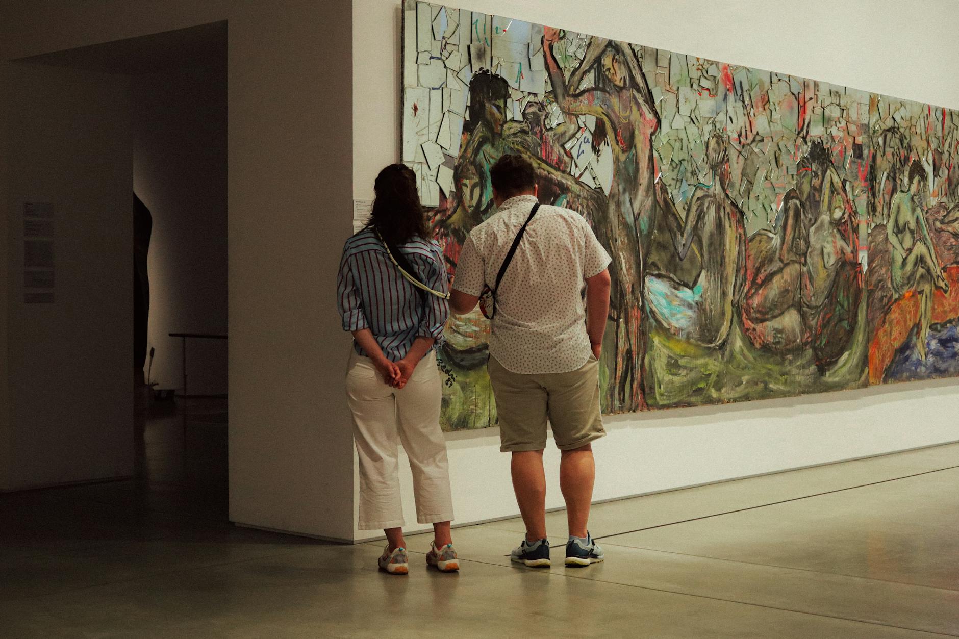 A visitor viewing paintings hung on a white gallery wall inside an art museum.