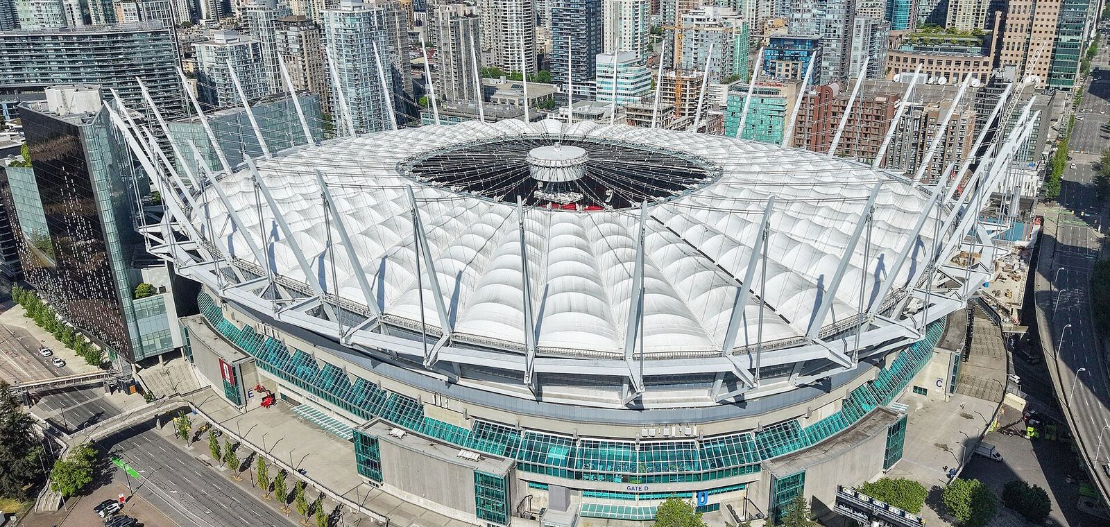 Aerial view of BC Place's white roof and masts with the downtown Vancouver towers behind