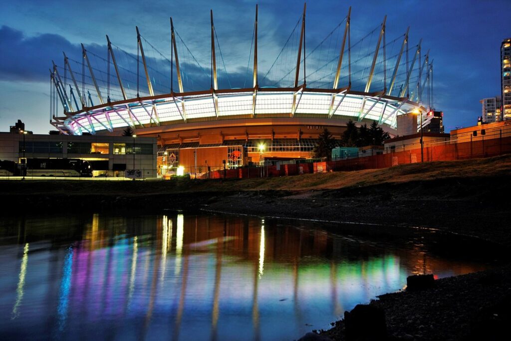 BC Place's lit roof masts reflected in False Creek at dusk, a view from any BC Place Stadium guide