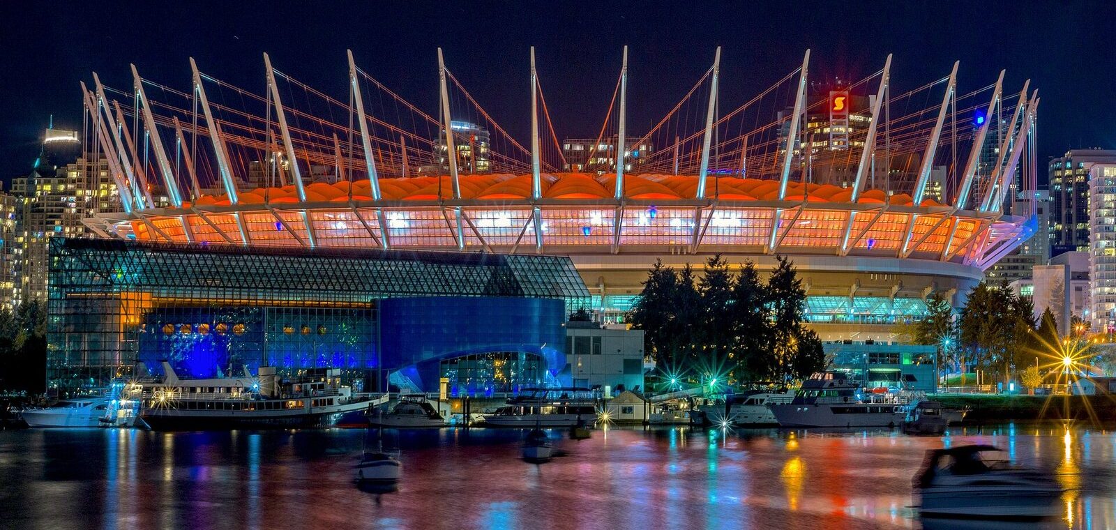 BC Place stadium lit orange at night, its roof masts reflected in False Creek