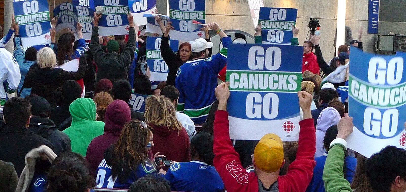 Crowd of Canucks fans holding Go Canucks Go signs and wearing team jerseys