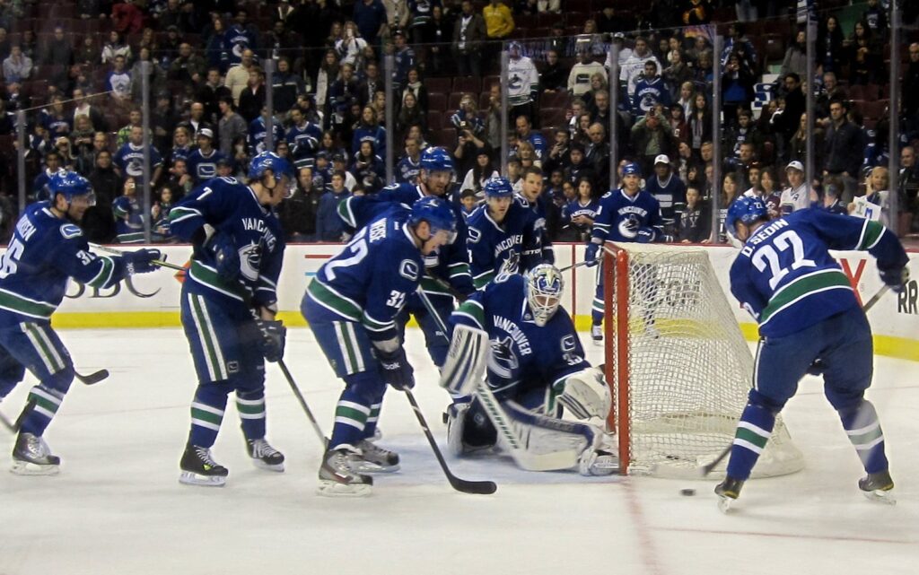 Canucks players in blue home jerseys crowding the goal during pre-game warm-ups