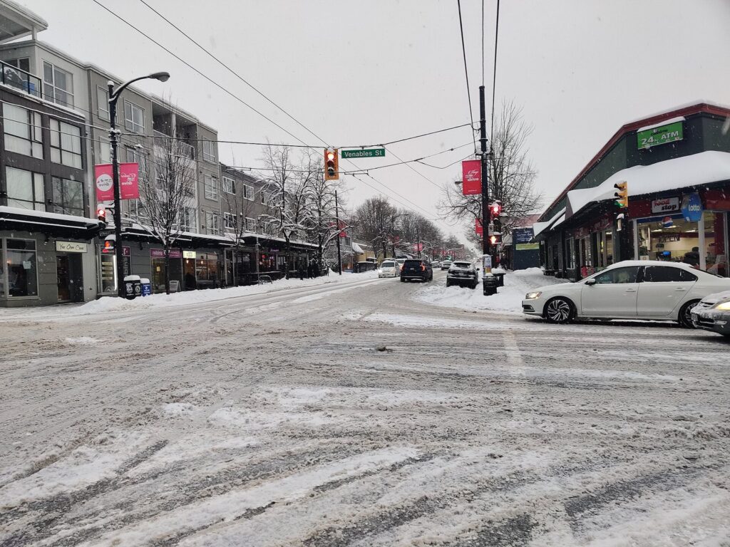Commercial Drive storefronts, banners and trolleybus wires under fresh snow
