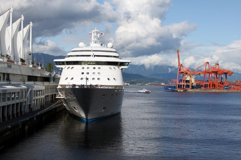 A white cruise ship docked at the Canada Place cruise terminal in Vancouver Harbour with the North Shore mountains behind