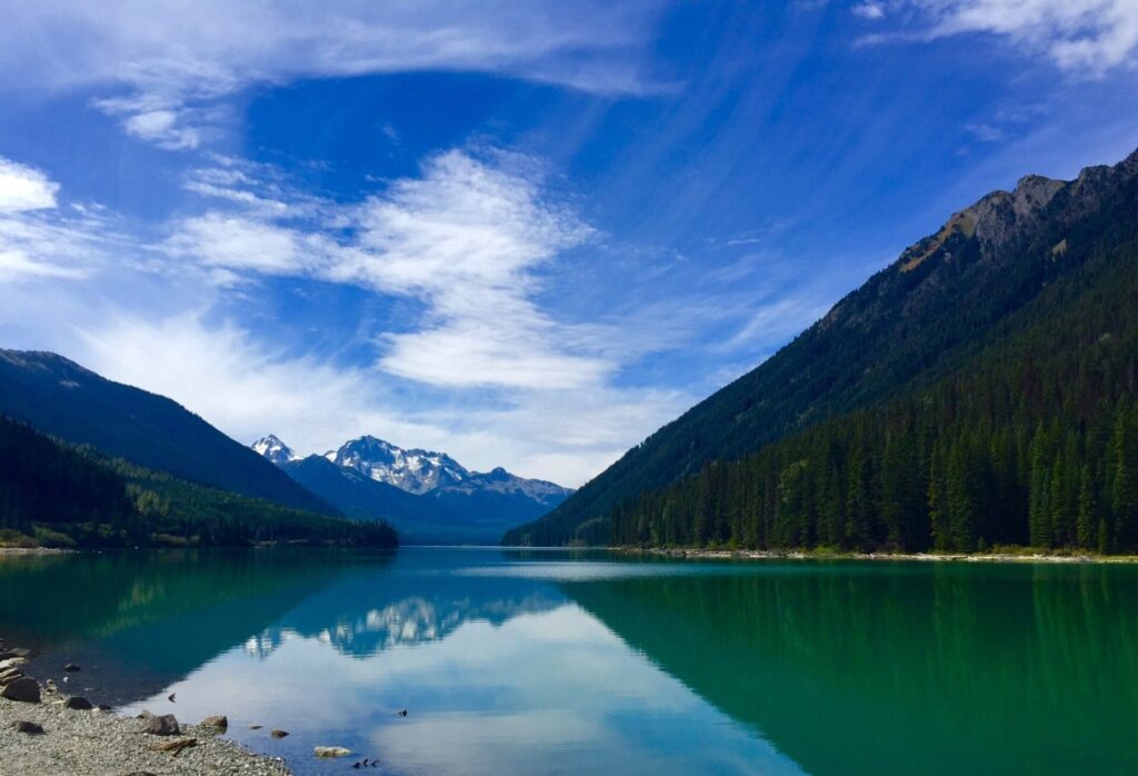 Duffey Lake reflecting forested slopes and snow-capped peaks under a blue sky