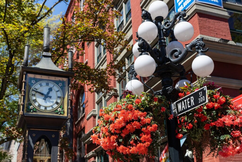 Gastown steam clock beside a Water Street sign and hanging baskets of red flowers