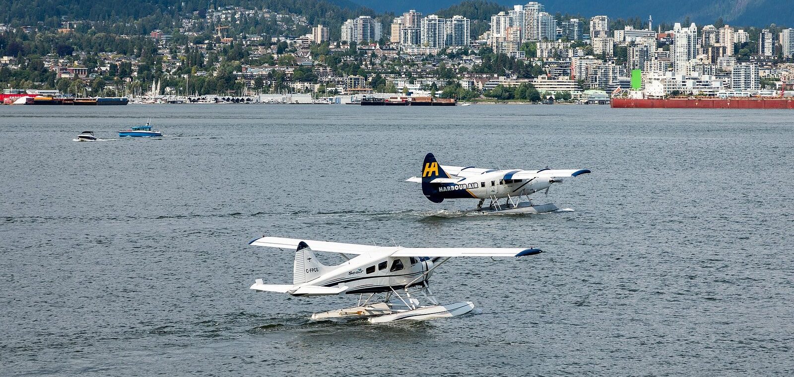 Two Harbour Air floatplanes taxiing on Vancouver Harbour with North Vancouver behind