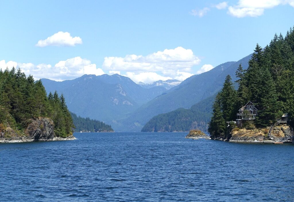 Forested islands and mountains along the Indian Arm fjord under a blue sky