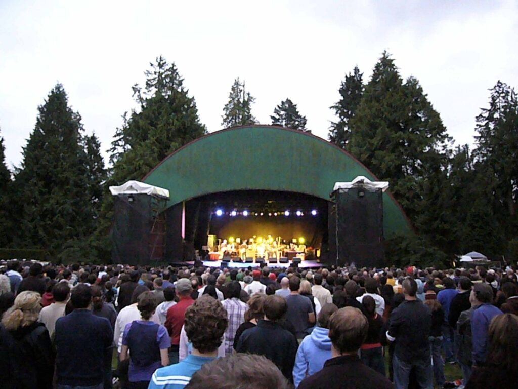 Crowd on the lawn in front of the green shell of Malkin Bowl in Stanley Park during a concert