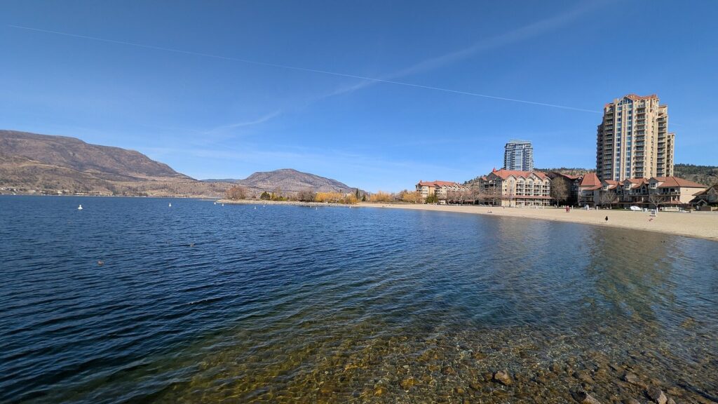 Clear water and a sandy shore on Okanagan Lake at Kelowna with hills beyond