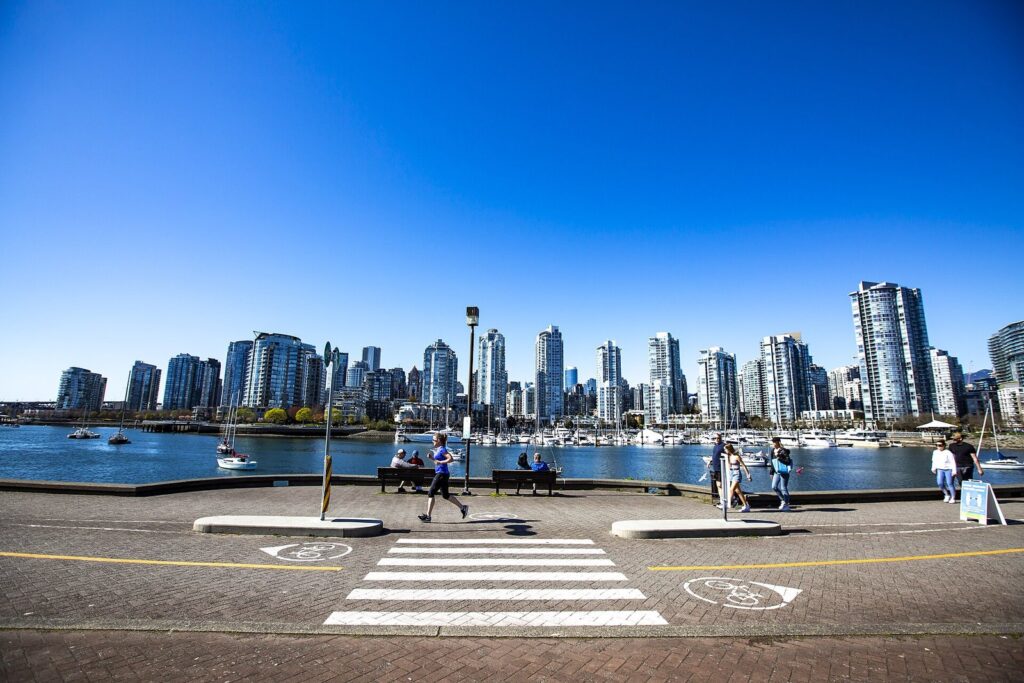 People on the wide seawall at Olympic Village with the downtown towers and False Creek behind