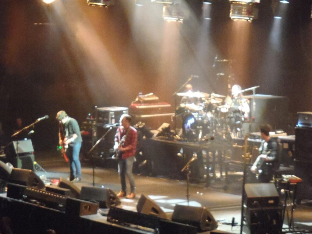 Band performing on a lit stage at one end of Rogers Arena with the crowd in the lower and upper bowls