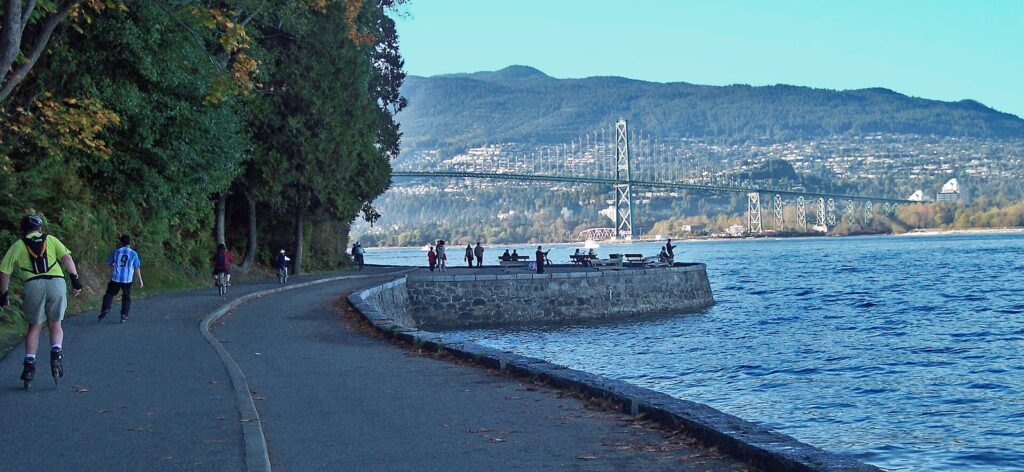 Walkers and inline skaters on the Stanley Park Seawall with Lions Gate Bridge behind
