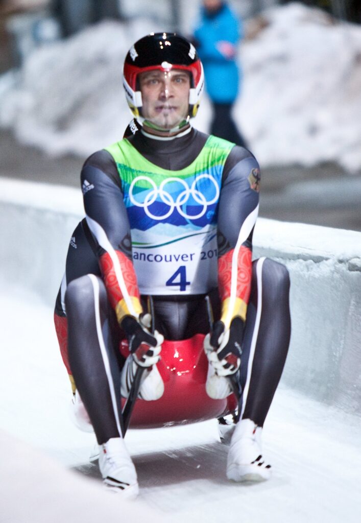 A luge athlete in a Vancouver 2010 race bib sliding feet first down the icy Whistler track