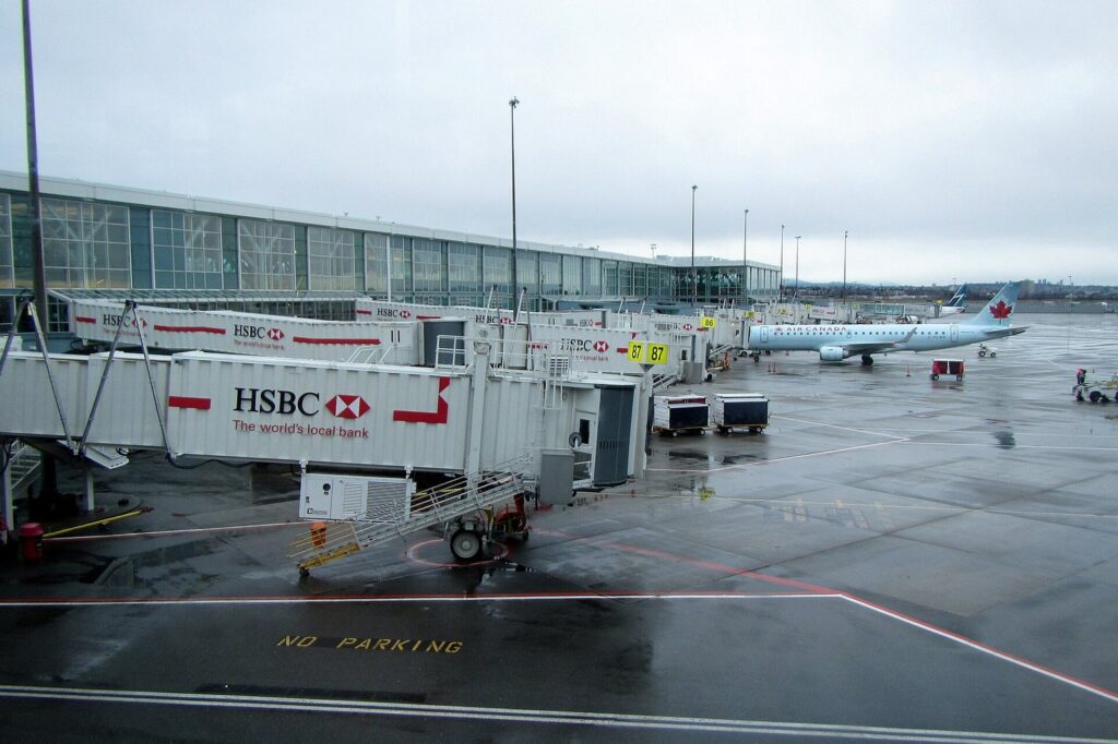 Rain-soaked apron at Vancouver International Airport with jet bridges and an Air Canada jet taxiing past